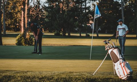 People on the golf course with a golf bag standing on the side.