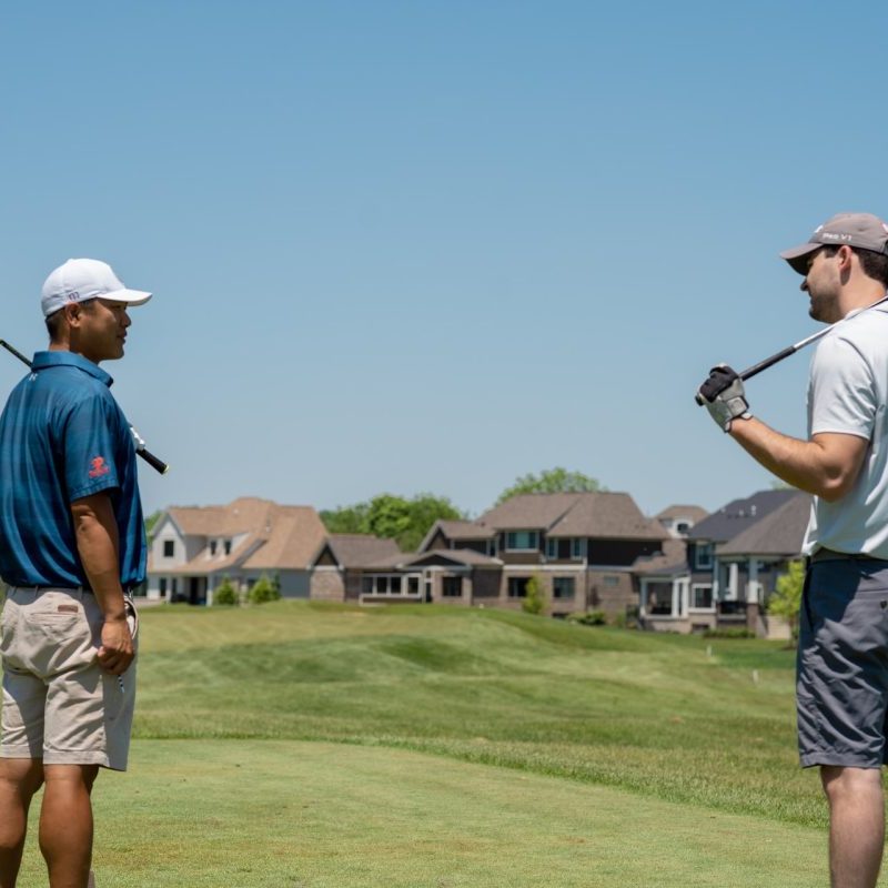 Two people looking at each other while holding their golf clubs over their shoulders.
