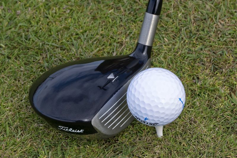 A three wood next to a ball on a tee.