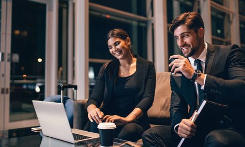Businessman and business woman looking at laptop in airport lounge