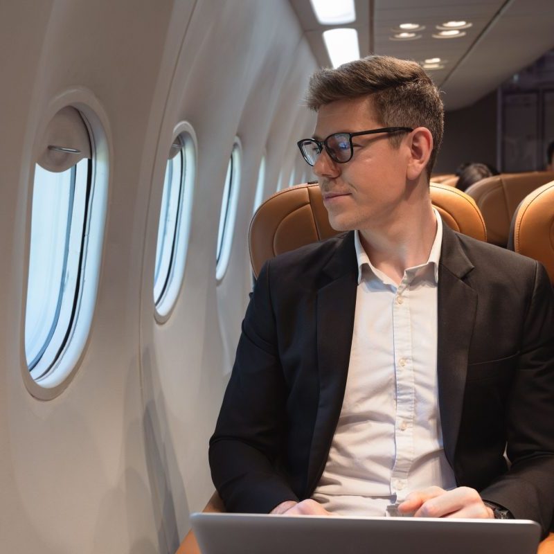 Man sitting in airplane looking out window with a laptop in his lap.