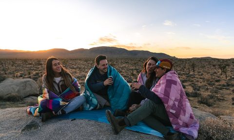 Three people wearing Rumpl Outdoor Blankets in the desert.