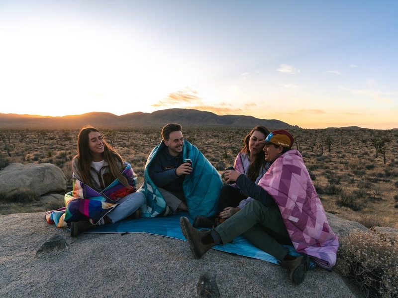 Three people wearing Rumpl Outdoor Blankets in the desert.
