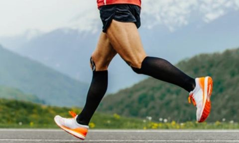 Runner wearing black compression socks while running with a mountain background scene.