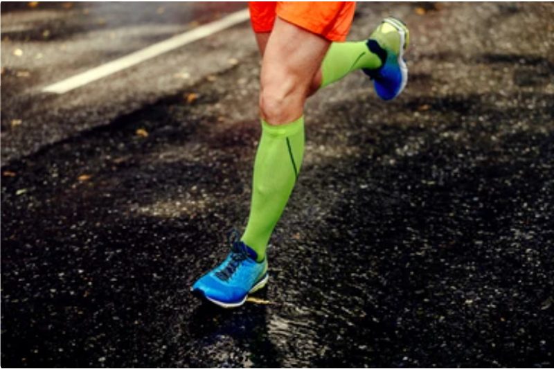 Runner wearing lime green compression socks while running on blacktop.
