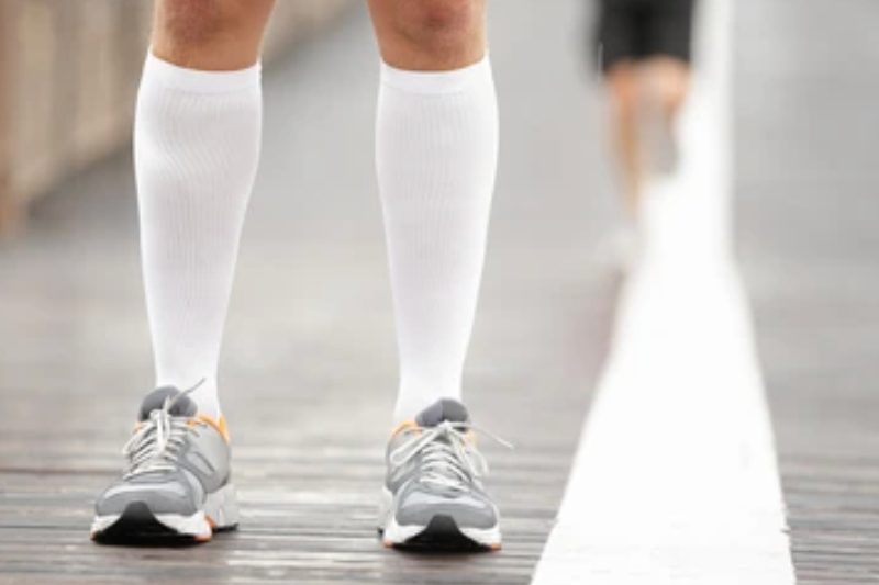 Runner wearing white compression socks standing on a wooden bridge.