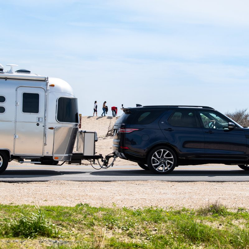 Airstream Caravel travel trailer being towed by an SUV near the beach.