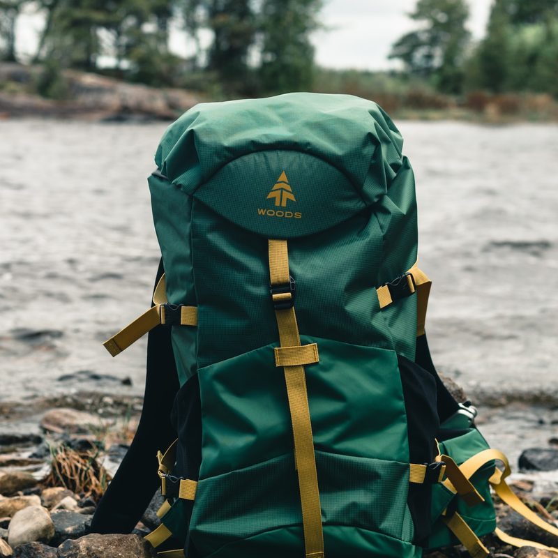 One green backpack on a brown wooden log in the woods.