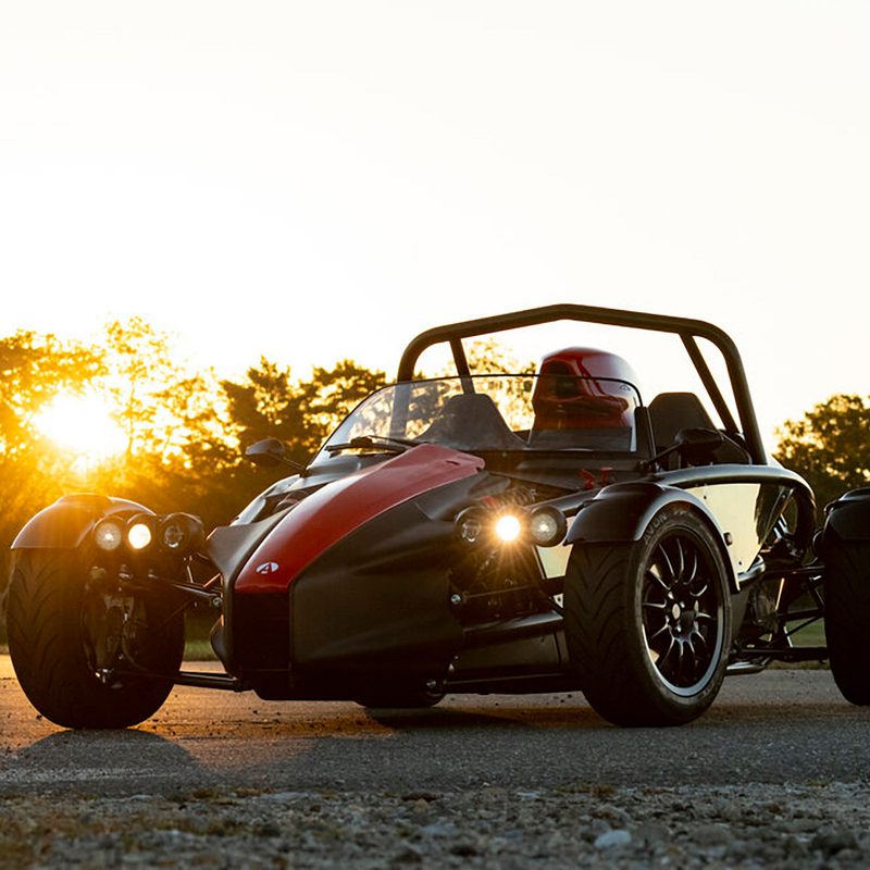 Ariel Atom 4 open-cockpit racecar, parked with sunset in the background.