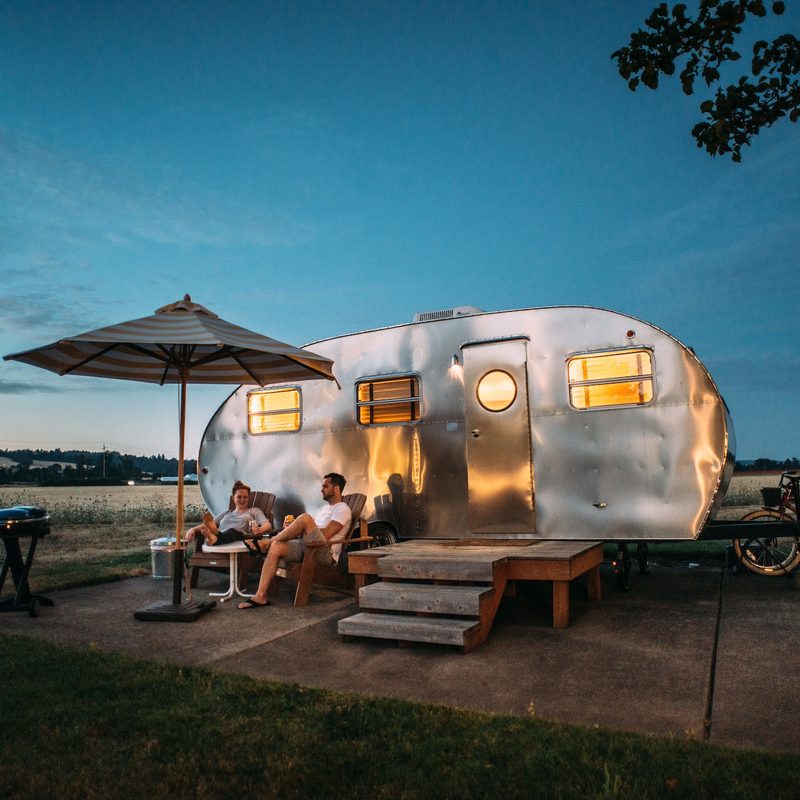 Young couple sitting outside a vintage aluminum travel trailer at night.