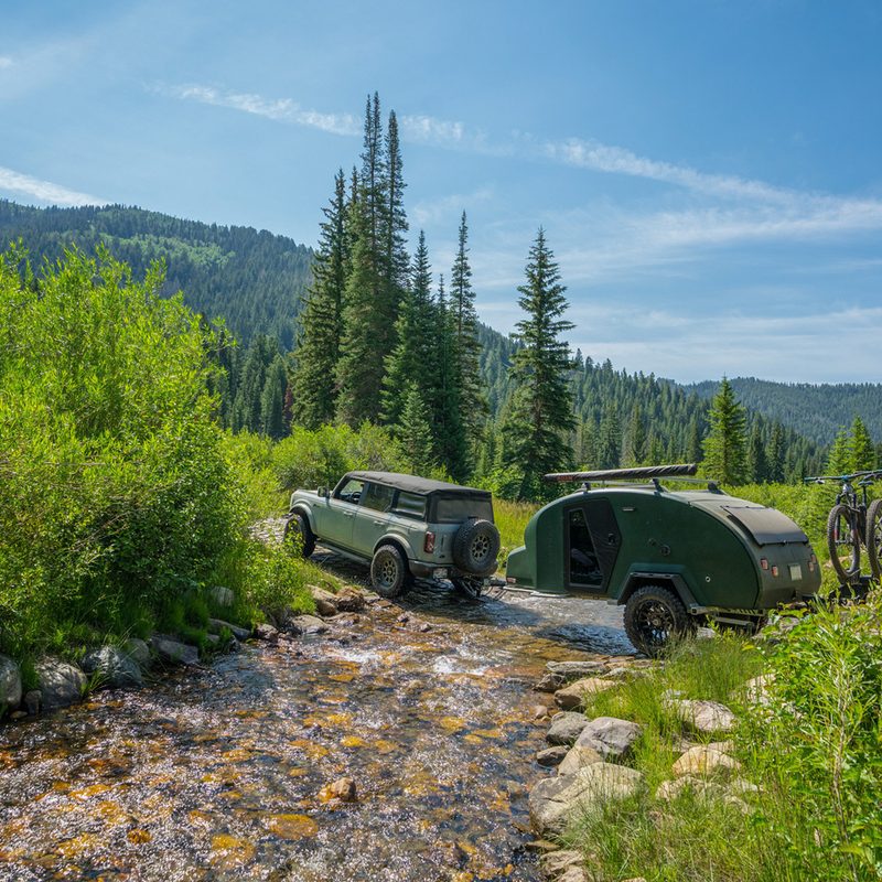 Ford Bronco towing Escapod TOPO2 Teardrop Trailer through a backcountry stream.