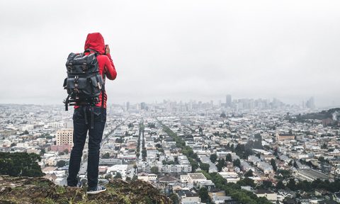 Hiker in a red hoodie taking photos overlooking San Francisco, California.