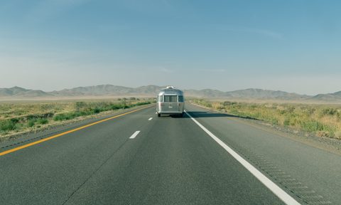 Long shot of the rear of an Airstream travel trailer being towed down a wide-open desert road.