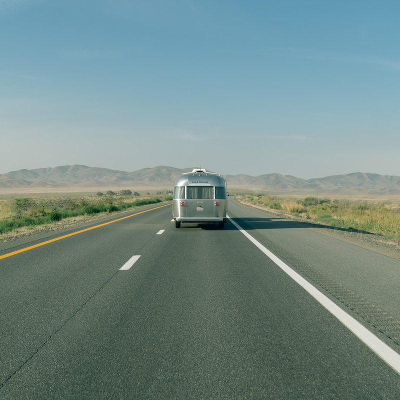 Long shot of the rear of an Airstream travel trailer being towed down a wide-open desert road.