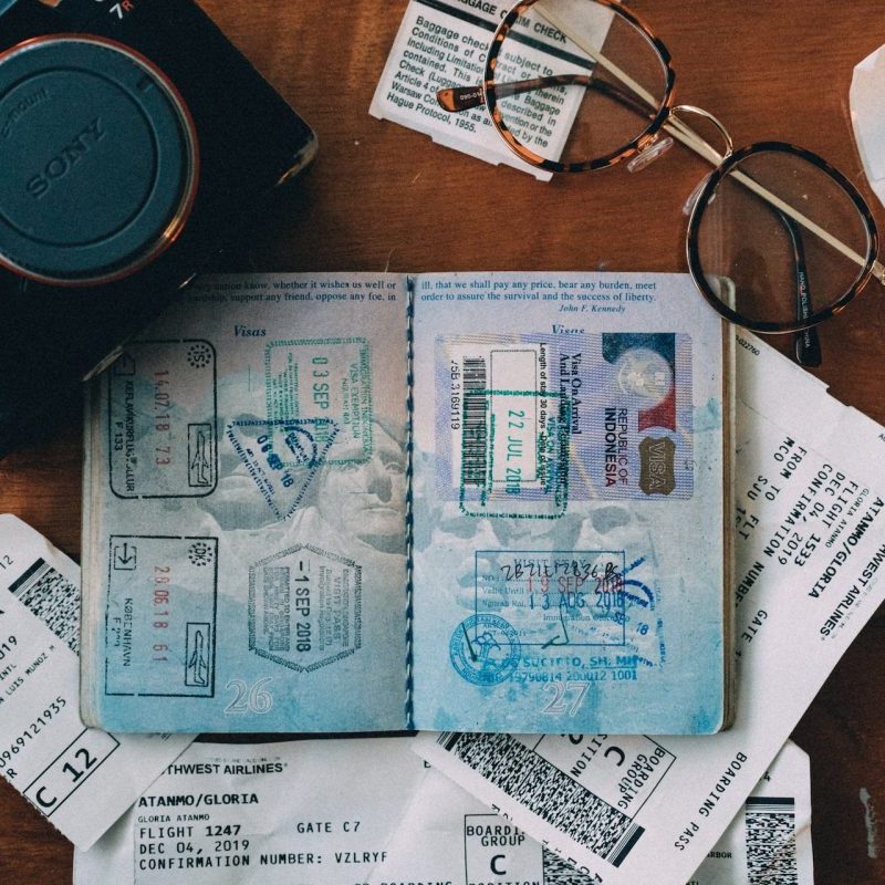 An open passport on a table with a pair of glasses and a camera around it