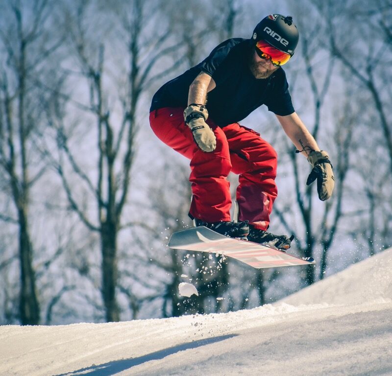 A man in a T-shirt snowboards in spring
