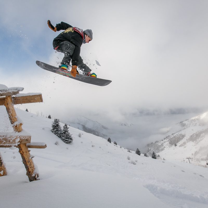A man jumps off a picnic table on a snowboard