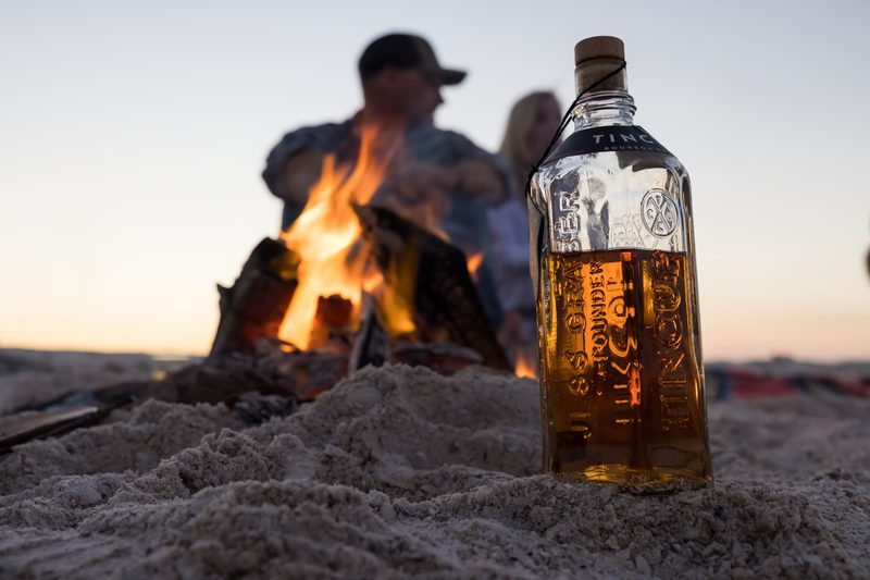 A group of people enjoy a bottle of TINCUP whiskey at the beach.