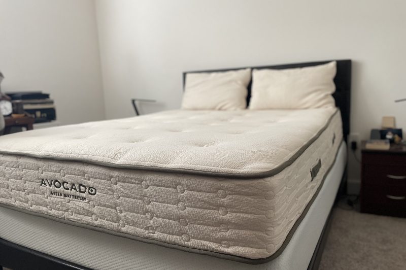 Stripped down Avocado mattress showing a low angle side shot on a bedframe next to a night stand and lamp.