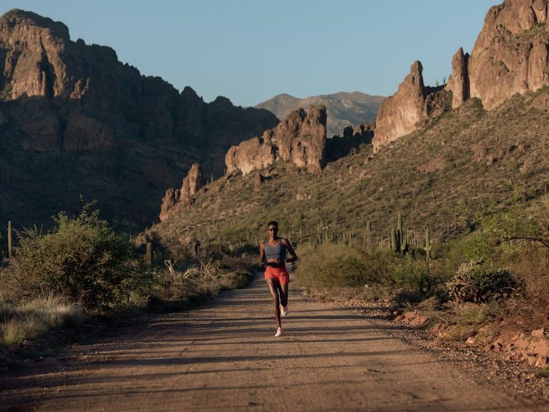 A runner on a dusty track with scrubland and rocky outcrops in the background.