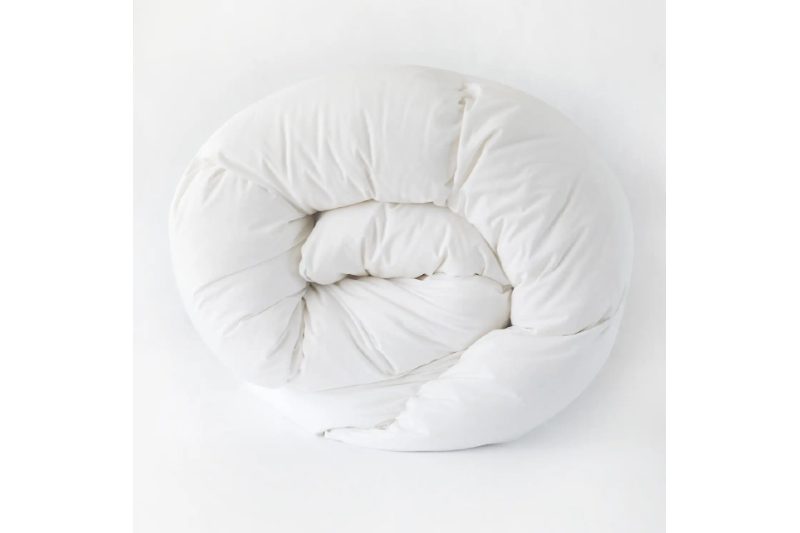 Quince Premium Down Comforter rolled up on a light gray background.