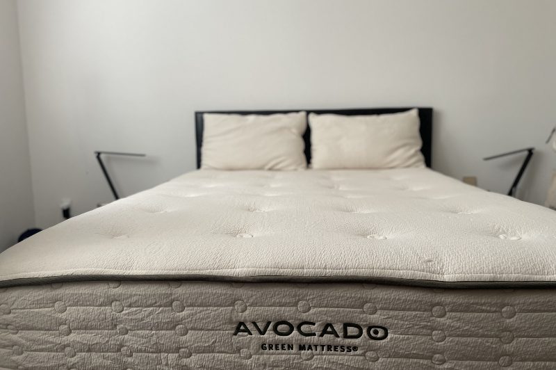 A stripped bed showing the avocado mattress and pillows next to two nights stands and lamps.