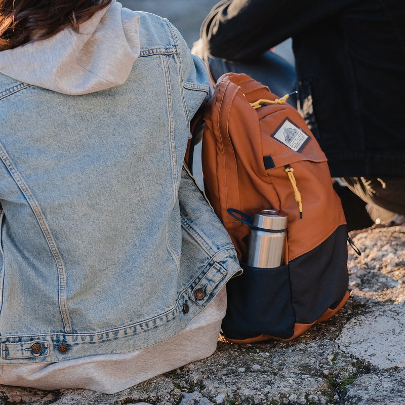 Woman in denim jacket sitting on a rock next to a daypack and a water bottle.