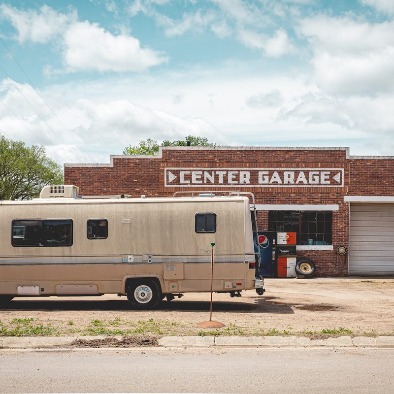 Old RV parked in front of a mechanic's garage.
