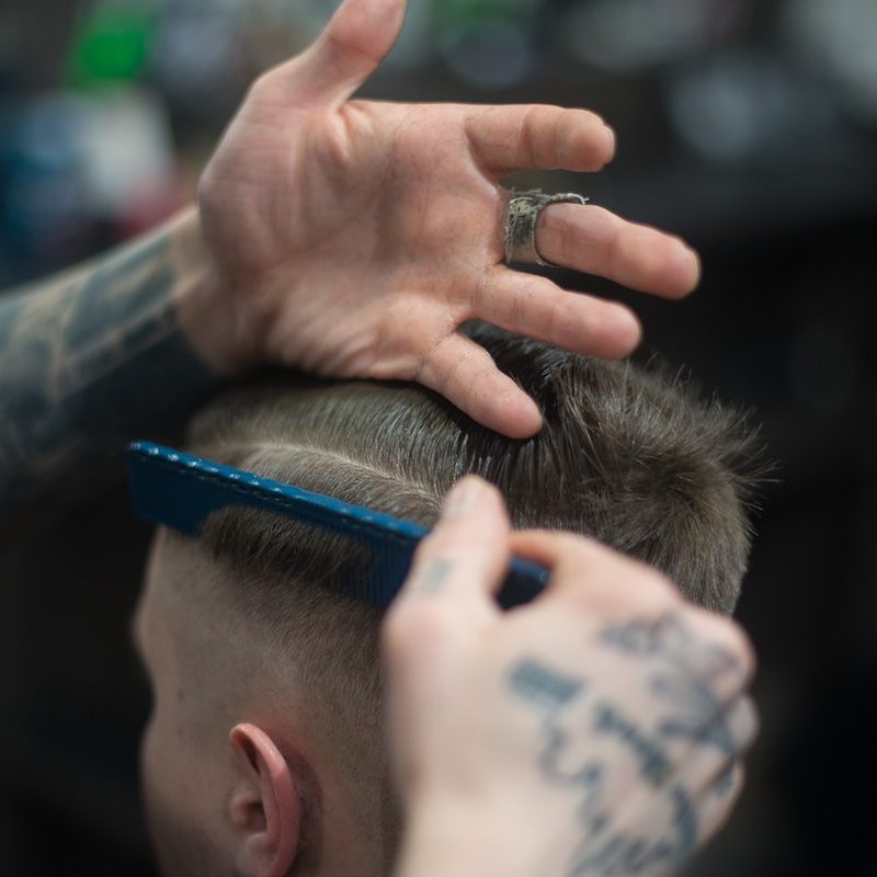 a man getting a haircut from tattooed barber