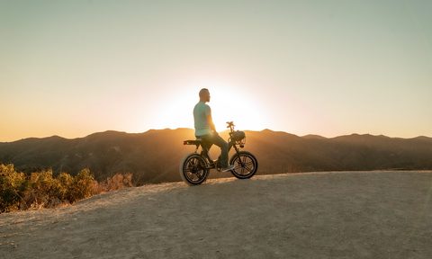 Man sitting atop an ebike with mountains and the setting sun in the background.