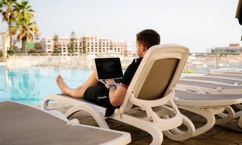 Young man relaxing with his laptop by a pool.