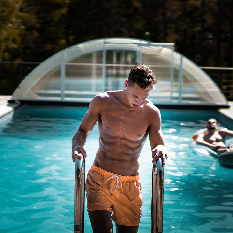 Fit, shirtless man climbing out of swimming pool.