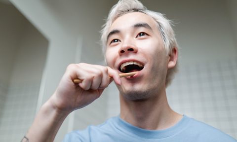 A man in a blue sweatshirt brushing his teeth