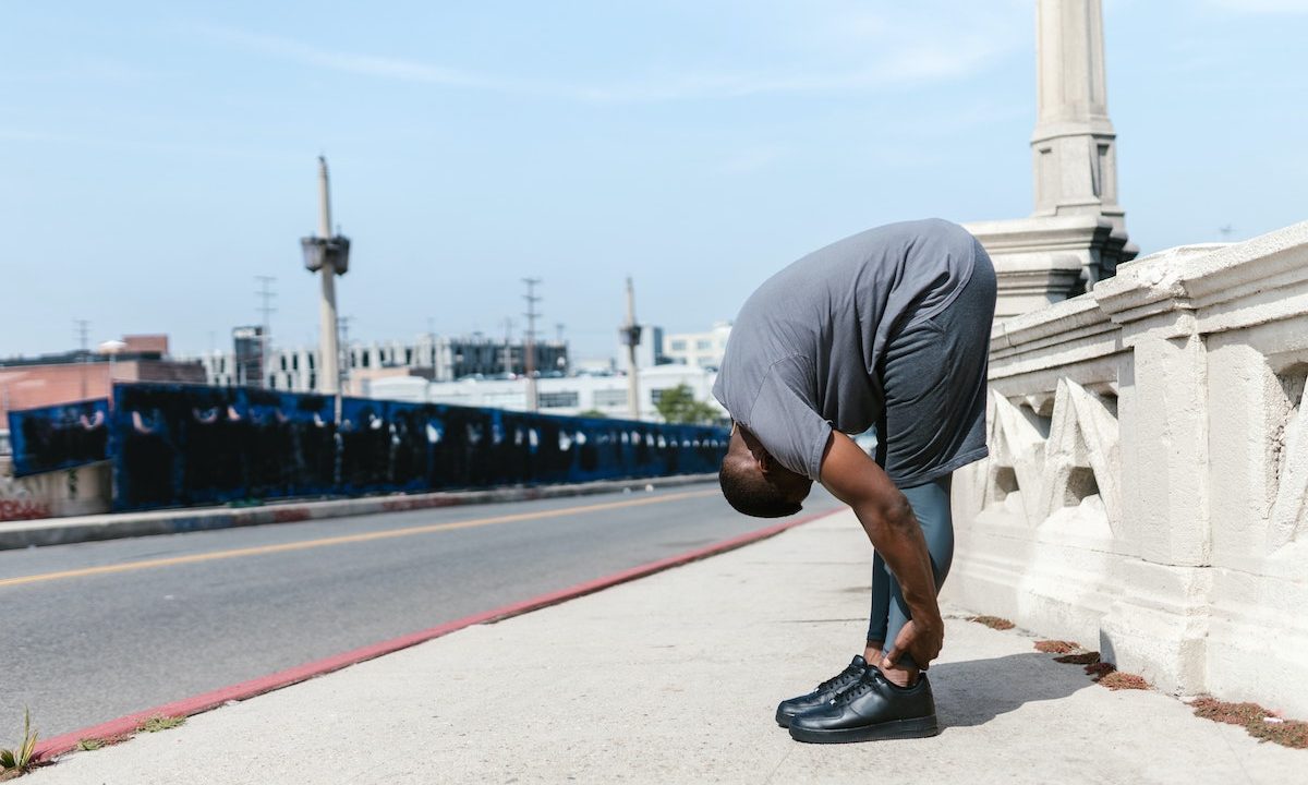 A man in gray shorts stretching on sidewalk