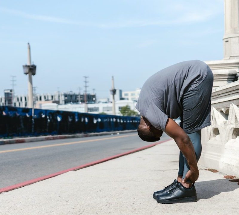 A man in gray shorts stretching on sidewalk