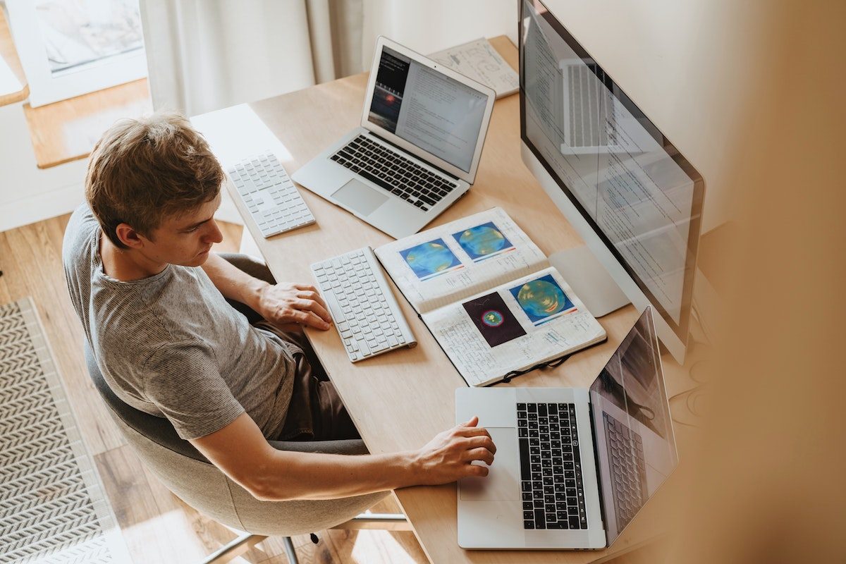man at wooden desk in front of 3 computer screens