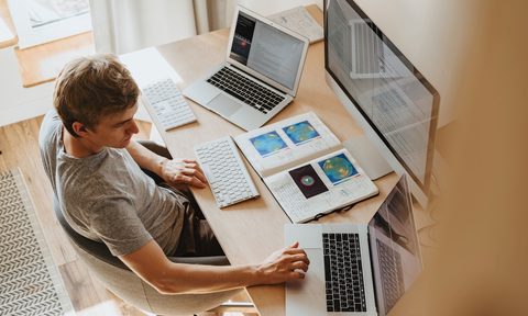 man at wooden desk in front of 3 computer screens