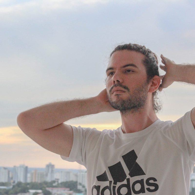 man standing on a rooftop in white adidas t-shirt and with a manbun