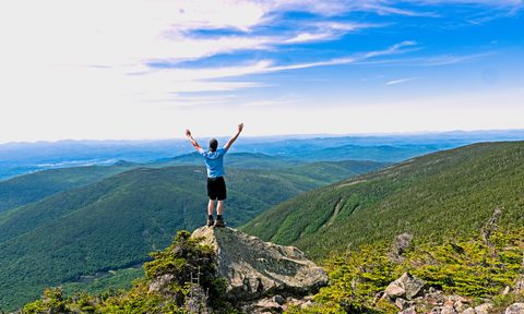Man standing triumphantly atop a peak in New Hampshire's White Mountain National Forest.