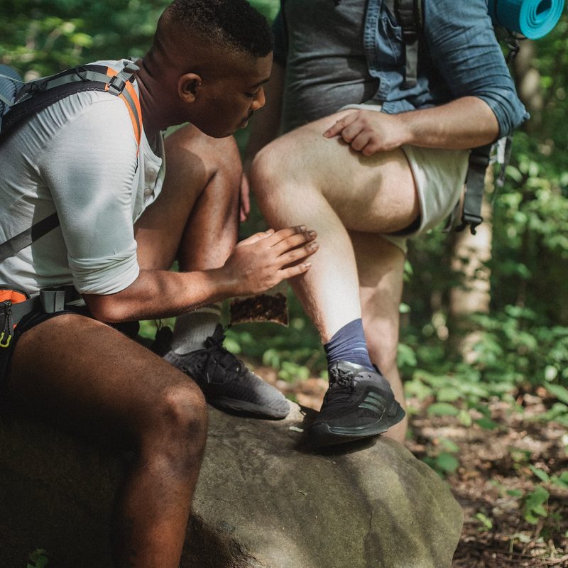 A man searches another man for ticks on the trail