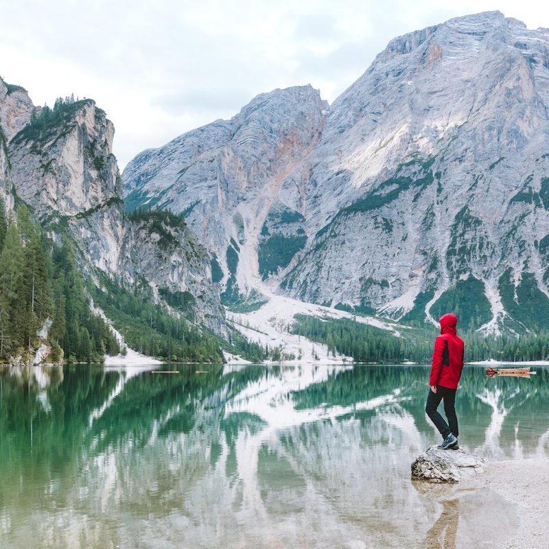 A man looks out over a lake surrounded by mountains and trees.