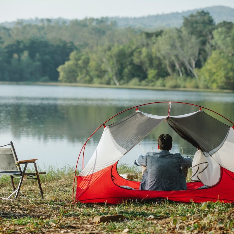 A man sits in the shade of a tent inner fly