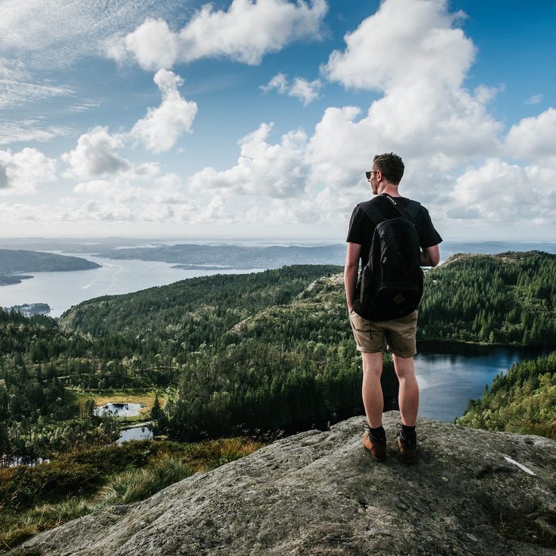 A man wearing a backpack stands on a rock overlooking a river valley.