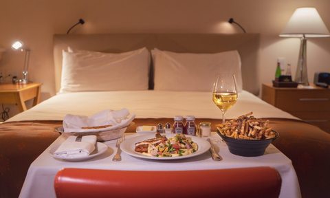A hotel room bed with room service tray at the foot.
