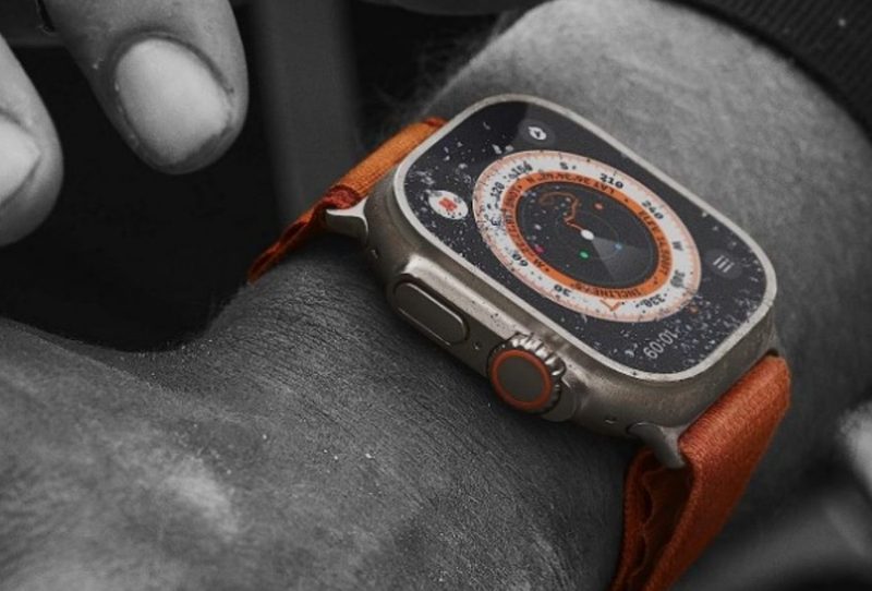 The Apple Watch Ultra covered in just a touch of sand on the arm of a man doing tough work.