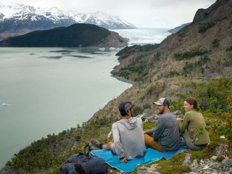 Three hikers sitting on a Rumpl Everywhere Mat overlooking a mountain lake.