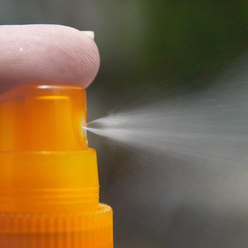 Closeup of a finger on the pump of a sunscreen spray bottle.