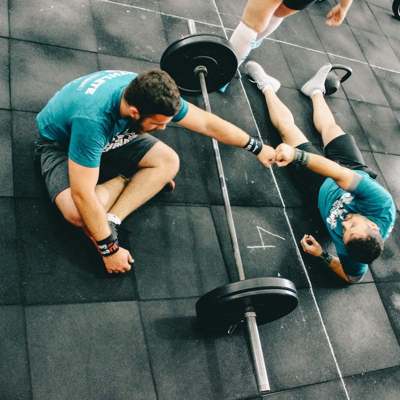 Man fist-bumping his personal trainer over a barbell.