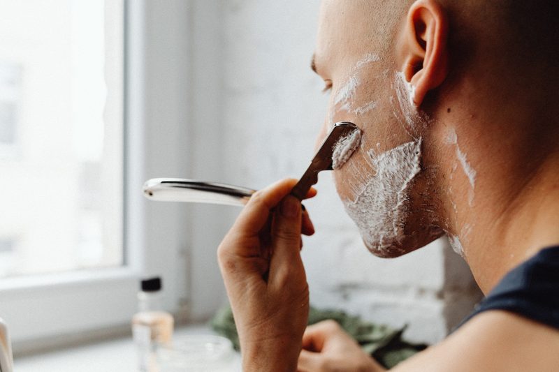 Bald man shaving face over sink