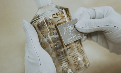 Someone sticking a label on a bottle of the Creed Aventus cologne.
